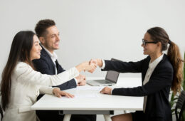 Smiling diverse businesswomen shake hands at group meeting, friendly asian hr handshaking congratulating hired applicant at job interview, satisfied millennial partners make contract deal concept